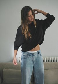 Czarna, oversize bluza z długimi rękawami, w zestawieniu z jasnoniebieskimi, wysokim stanem dżinsami. Miękka tkanina i casualowy krój, z luźnym fasonem.