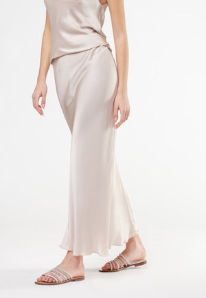 Top in satin beige chiaro e gonna fluida con una consistenza morbida. Modella che indossa sandali piatti con molteplici cinturini scintillanti.