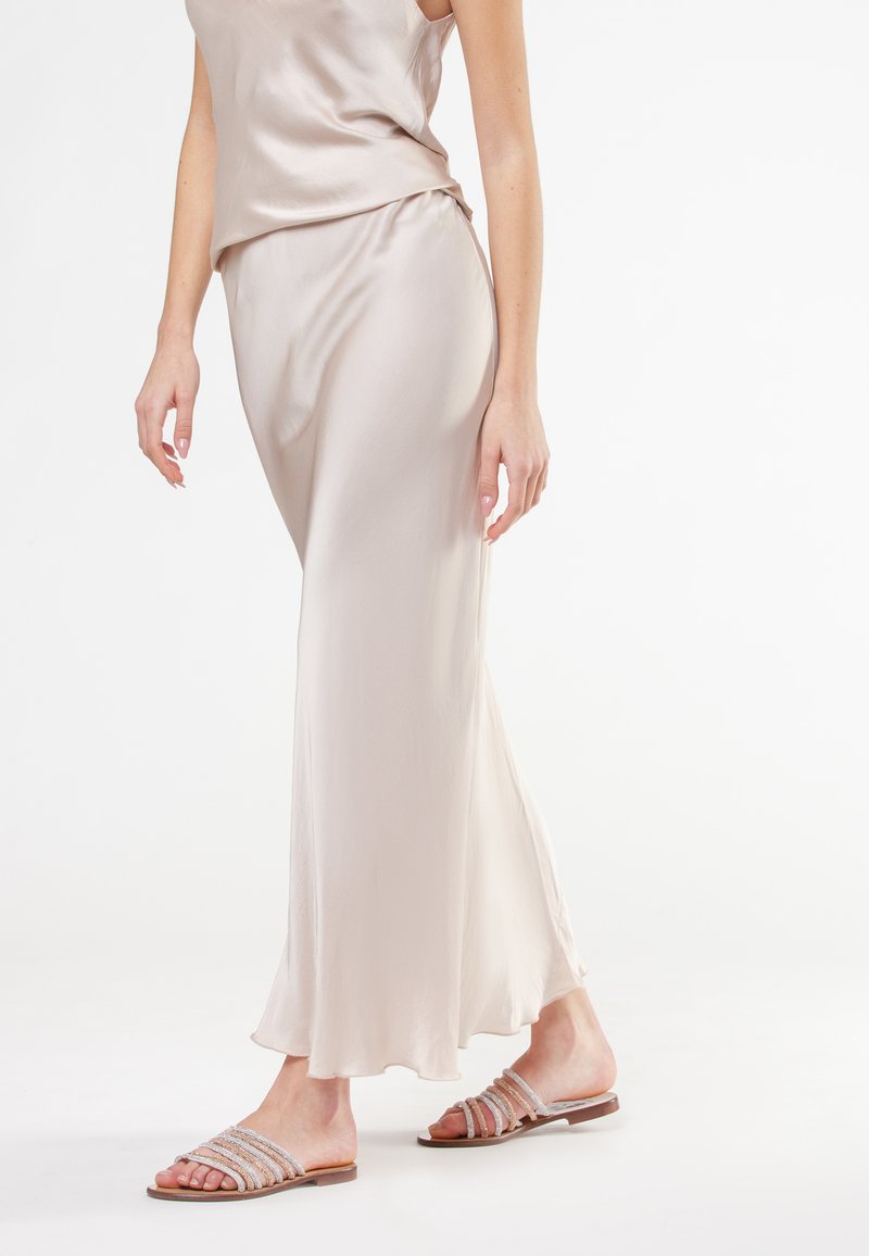 Top in satin beige chiaro e gonna fluida con una consistenza morbida. Modella che indossa sandali piatti con molteplici cinturini scintillanti.