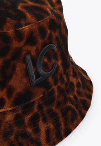 Hnědý klobouk s leopardím potiskem ve tvaru kýble, vyrobený z plyšového materiálu; na boku má vyšívané černé logo "LC". Měkká textura s širokým okrajem.