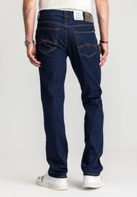 Ciemnoniebieskie jeansy z denimu o prostych nogawkach, z dwoma tylnymi kieszeniami i kontrastującym przeszyciem. W zestawieniu z białymi trampkami.