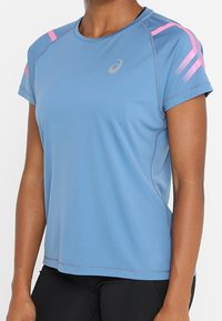 Camiseta deportiva de manga corta azul claro con detalles en rosa en los hombros, confeccionada con tejido que absorbe la humedad, con cuello redondo y corte holgado.