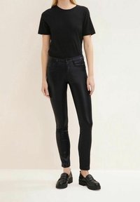 Schwarzes T-Shirt, kurze Ärmel, kombiniert mit schwarzen glänzenden Slim-Fit-Jeans. Das Modell trägt schwarze Slipper. Schlichtes, sauberes Design; keine sichtbaren Muster.