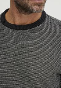 Suéter de punto con patrón a rayas en blanco y negro, con un cuello negro acanalado y tejido texturizado.