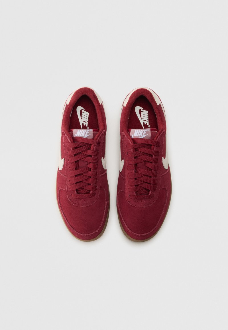 Baskets en daim rouge avec un profil bas, arborant des logos Nike swoosh blancs, des lacets plats et une semelle en caoutchouc naturel.