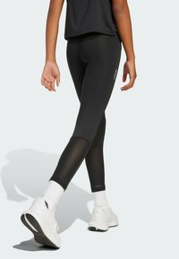Leggings noirs avec une texture lisse et des accents en maille, associés à des chaussures de sport blanches et des chaussettes de cheville visibles.