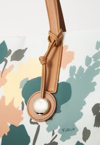 Sac fourre-tout floral avec un fond bleu clair, arborant des motifs floraux orange, vert et gris foncé. Poignée en cuir brun et détails accentués.