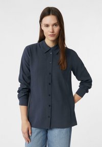 Ciemnoniebieska koszula z długim rękawem i klasycznym kołnierzykiem, wykonana z teksturowanej tkaniny. Charakteryzuje się prostym krojem i subtelnymi pionowymi liniami.