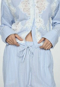 Vaaleansiniset ja valkoiset raidalliset pyjamakokonaisuudet, joissa on napitettavissa oleva paita, jossa on pitsiyksityiskohtia. Housuissa on nauhavyötärö. Rakennekangas.