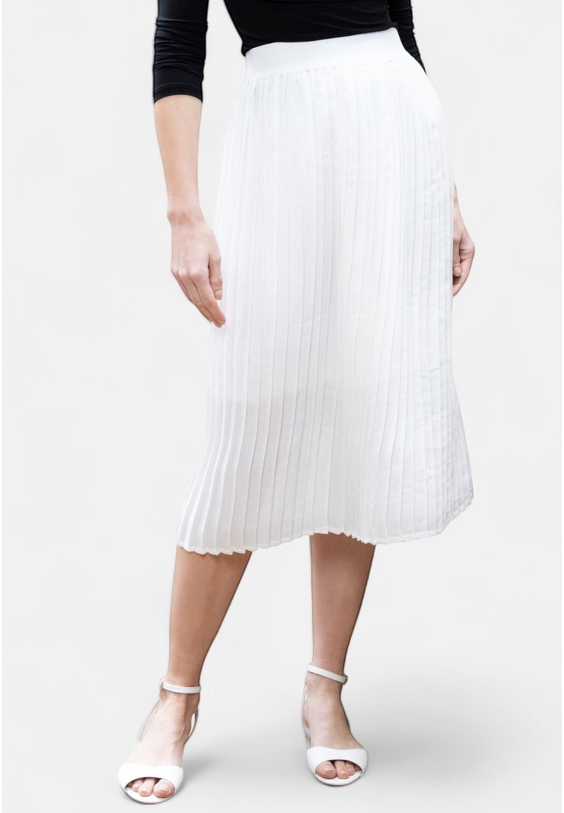 Jupe midi plissée blanche avec une texture lisse et un ourlet en forme de vagues. Associée à des sandales blanches à bout ouvert et un haut noir.