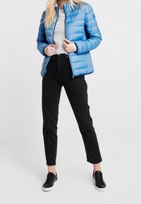 Jasnoniebieska kurtka puchowa z pikowanym wzorem, zestawiona z czarną i białą bluzką w paski, czarnymi, krótkimi dżinsami i czarnymi sneakersami.