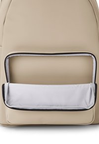 Beige hátizsák sima felszínnel, elöl cipzáras zsebbel, szürke béléssel és fekete cipzárral rendelkezik, kiemelve ezzel jól megtervezett formáját.