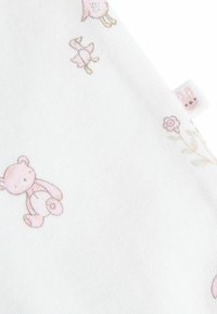 Tissu en coton avec un fond blanc présentant des motifs roses de ours, de fleurs et d'oiseaux. Comprend une petite étiquette avec un design de lapin.