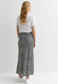 Jupe maxi en tissu noir avec des pois blancs, associée à un t-shirt blanc court et des baskets blanches. Texture lisse et design fluide.