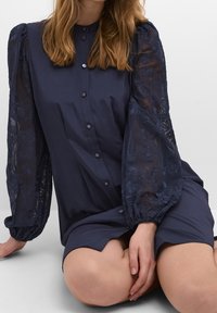 Marinblå skjortklänning med hög krage, knappslå och genomskinliga, puffiga spetsärmar med blomsterbroderi och samlade manschetter.