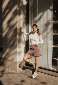 Vormgevende witte langwerpige top en lichtbruine shorts, gecombineerd met grijze sneakers. De shorts hebben een elastische tailleband.