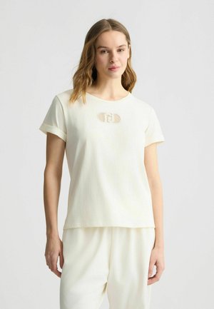Cream-colored short-sleeve t-shirt with a round neckline and a textured logo detail in the center. Soft fabric with a relaxed fit.