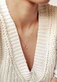 Collier pendentif en lune croissante en or rose sur une délicate chaîne, porté avec un épais pull blanc en tricot ayant une texture côtelée.