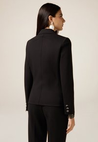 Czarna, dopasowana marynarka o eleganckim kroju, gładkiej fakturze i guzikach na rękawach. Widok z tyłu pokazujący strukturalny design i szwy.