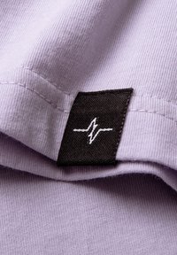 Light purple cotton fabric with a textured surface. Features a black label at the edge showcasing a white zigzag logo.