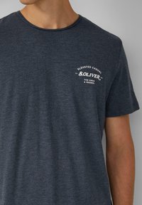 Donkerblauwe katoenen T-shirt met ronde hals, voorzien van een wit logo op de linkerborst dat "S.OLIVER." zegt. De stof heeft een subtiele textuur.