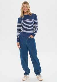 Námornícky pruhovaný sveter s svetlomodrými pruhmi, okrúhly výstrih, rebrované manžety, spárovaný s voľnými modrými džínsami a béžovými teniskami.