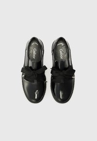 Chaussures en cuir verni noir avec un bout rond, ornées d'un grand nœud noir et d'une semelle texturée. La doublure et la semelle intérieure sont lisses.