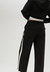 Černé kalhoty rovného střihu, zdobené bílými bočními pruhy, zadními kapsami a elegantním pasem. Vyrobeno z hladkého materiálu.