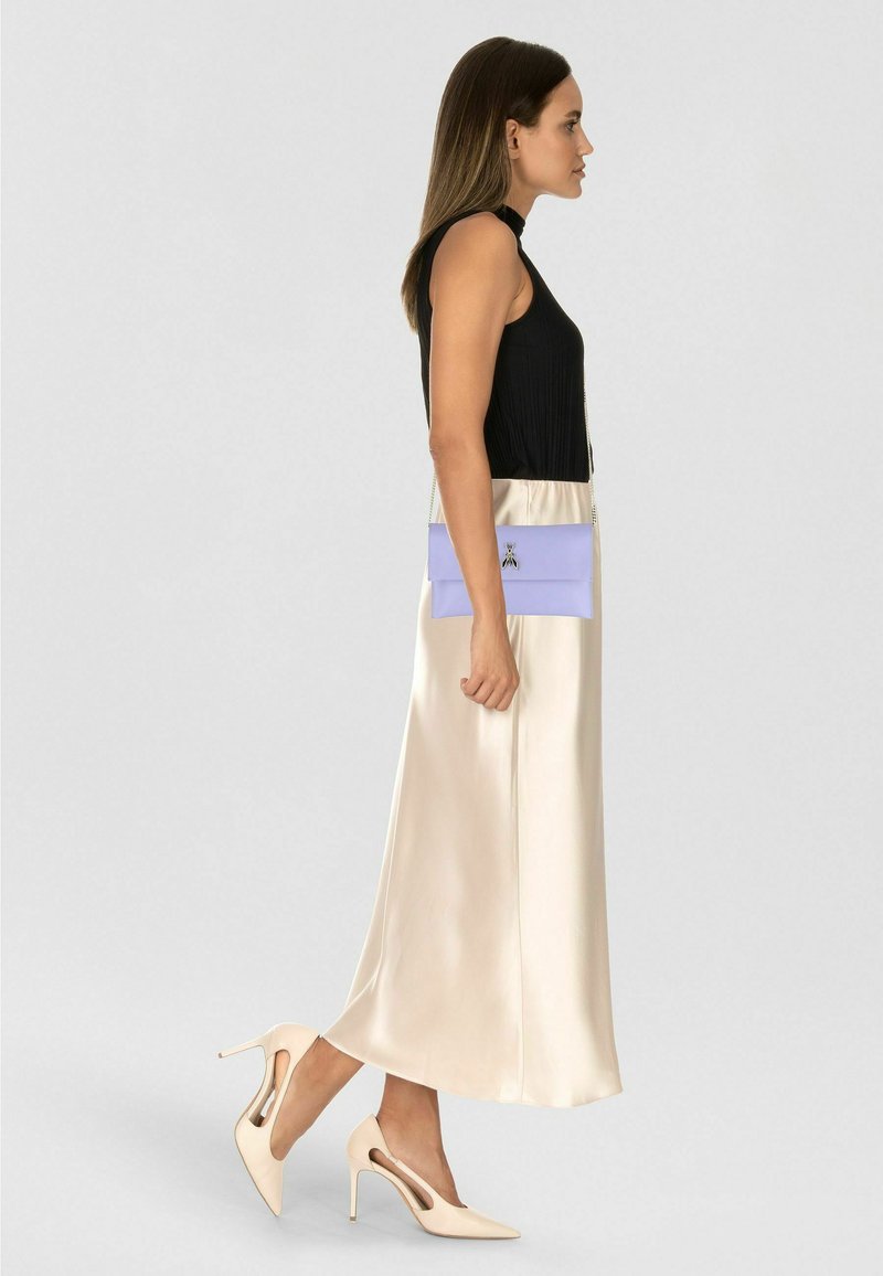 Schwarzes, geripptes ärmelloses Oberteil, beiger langer Satinenrock, lavendelfarbene Clutch mit silberner Kette und beige High Heels mit Cut-out-Details.