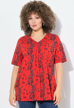 Haut rouge à manches courtes avec un décolleté en V, motifs textuels noirs sur l'ensemble et une coupe ample. Le texte se compose de diverses lettres dans une disposition ludique.