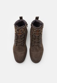 Bottines en daim marron avec un bout rond, un laçage à l'avant et une doublure en tissu rayé contrasté. Présentent des œillets en métal et une languette en boucle au niveau du talon.