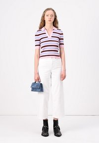 Ραβδωτή, κοντομάνικη πλέξη σε ροζ, μπλε και καφέ χρώμα; σε συνδυασμό με λευκά παντελόνια με φαρδιά πόδια. Κρατώντας μια μικρή μπλε σουέτ τσάντα. Μαύρες μποτες μέχρι τον αστράγαλο.