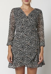 Schwarzes Blumen-Wickelkleid mit langen transparenten Ärmeln. Verfügt über einen V-Ausschnitt, zarte Blumenmuster und einen schwingenden Rock. Weicher Stoff.