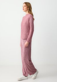 Szydełkowy dwuczęściowy zestaw w miękkim różu, zawierający sweter z wysokim kołnierzem i długim rękawem z fakturowanym wzorem w diamenty oraz luźne spodnie.