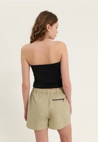 Svart tube-top kombinert med lysebeige shorts med elastisk linning og en liten svart glidelåslomme bak.
