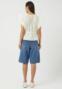 Wit top met vlindermouwen en een gerimpelde taille, gecombineerd met knie-lange blauwe denimshorts, met een relaxte pasvorm en een lichte textuur.