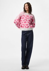 Pink and white knitted sweater with a floral pattern, loose fit, rounded neckline, paired with dark blue wide-leg jeans and black boots.