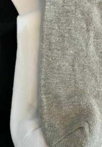 Three pairs of socks: black, white, and gray. The gray sock has a textured appearance, while the others are smooth with ribbed cuffs.