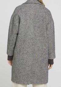 Cappotto grigio a spina di pesce con colletto, vestibilità oversize e polsini a maglia rigata. Tessuto testurizzato con una miscela di fili chiari e scuri.