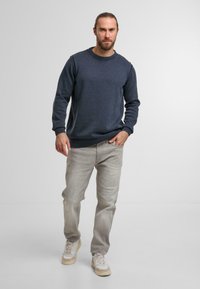 Dunkelblauer Pullover mit einem gerippten Ausschnitt und Bündchen, kombiniert mit hellgrauen Jeans und beigen Sneakers, in einem lässigen Schnitt und mit schlichtem Design.