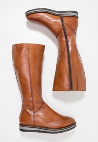 Bottes en cuir marron hautes jusqu'au genou avec une texture lisse, dotées d'une fermeture éclair sur le côté et d'une semelle en caoutchouc noire avec une rayure grise.