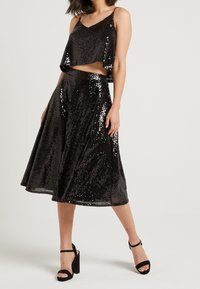 Black sequined two-piece outfit featuring a cropped top with thin straps and a knee-length flared skirt, finished with a smooth texture.