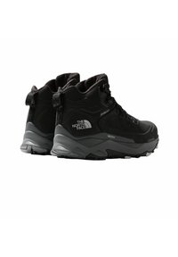 Czarne buty trekkingowe z teksturowaną cholewką, gumową podeszwą i średnią wysokością za kostkę. Charakteryzują się sznurowaniem i akcentami z logo marki.