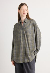 Camicia a quadri grigia e gialla con due tasche sul petto, vestibilità ampia, maniche lunghe e orlo curvo, realizzata in un tessuto testurizzato.