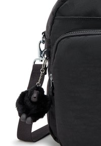 Black fabric backpack with a smooth texture, featuring a zipper pocket and a keychain accent of a fluffy black gorilla.