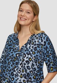 Leopardprint blouse in lichtblauw, met korte mouwen, een V-halslijn en een textuurstof met zwarte en gele accenten.