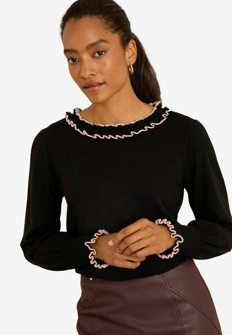 Must mustreptikk ja roosade volangidega kaeluse ja varrukate ääred, näidates slim-fit disaini ja pehmet tekstuuri.