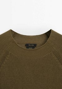 Gros plan sur l'encolure d'un pull tricoté vert olive avec une étiquette visible indiquant 100 % lin et le nom de la marque.