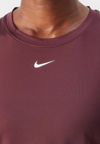 Gros plan sur une personne portant un t-shirt Nike bordeaux avec un logo swoosh blanc centré sous l'encolure.
