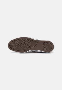 Suela de zapato de goma marrón con un patrón geométrico y superficie texturizada. Los bordes cuentan con un acabado en blanco; son visibles surcos para tracción.